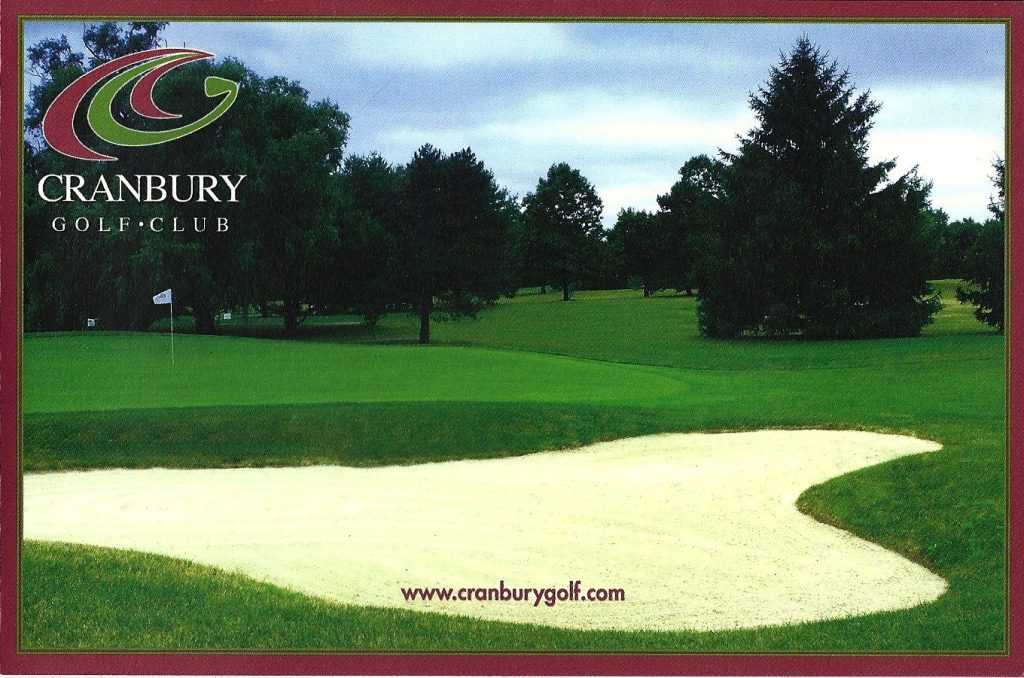 View of a golf course at Cranbury Golf Club featuring a sand trap in the foreground and lush green grass in the background.